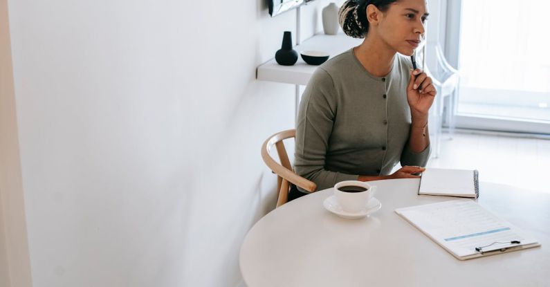 Task Manager - Concentrated ethnic female HR interviewer or psychologist in formal clothes sitting at round table with pen and notepad while looking away in contemplation