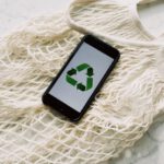 Save Icon - Overhead of smartphone with simple recycling sign on screen placed on white eco friendly mesh bag on marble table in room