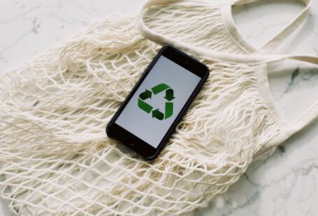 Save Icon - Overhead of smartphone with simple recycling sign on screen placed on white eco friendly mesh bag on marble table in room